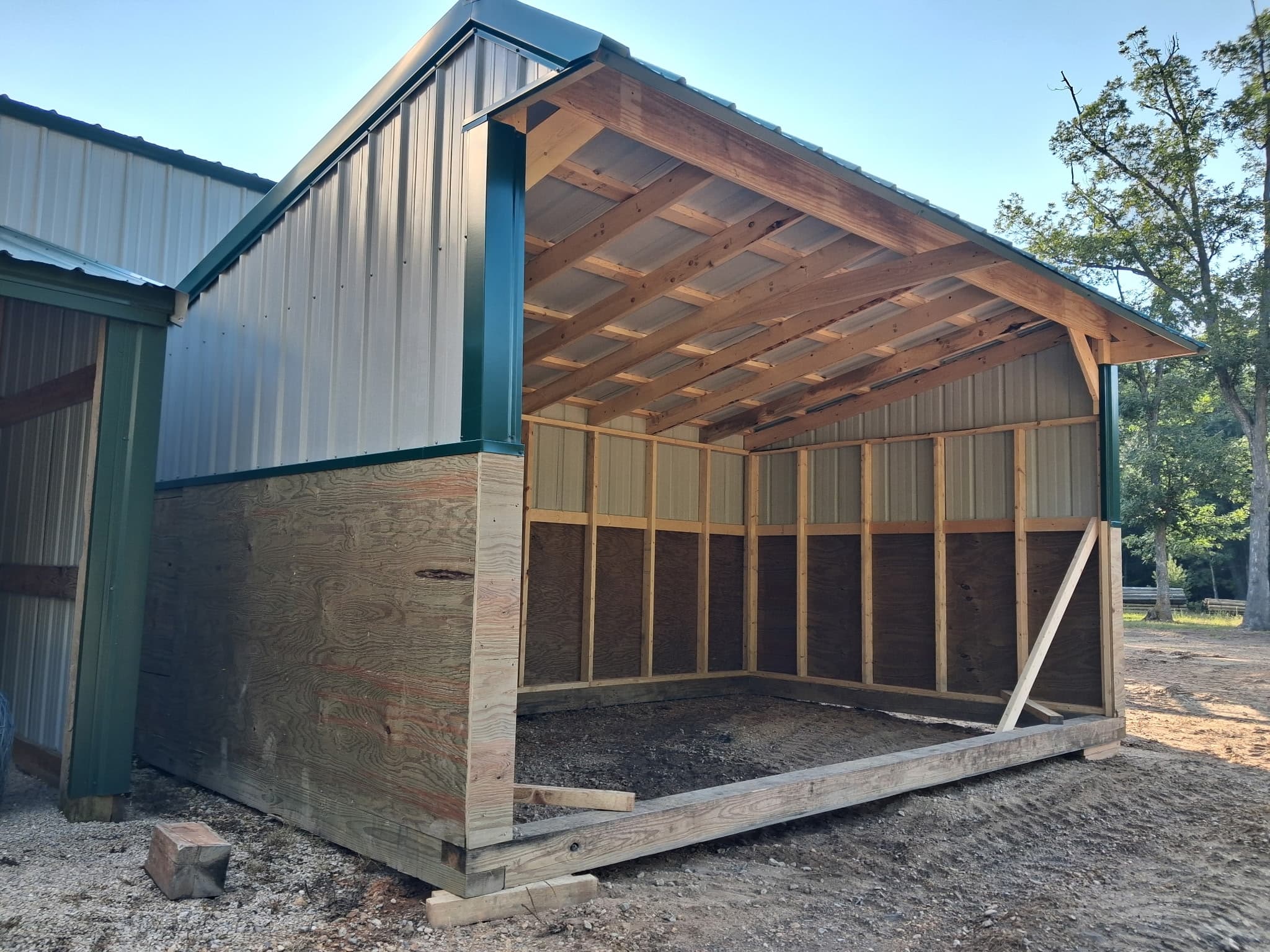 Close view of a gray horse shelter with green trim and exposed wood framing.