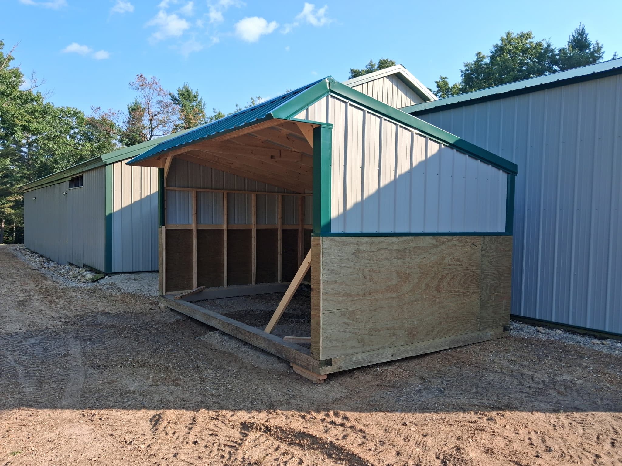 Gray custom horse shelter with green trim beside a farm building.