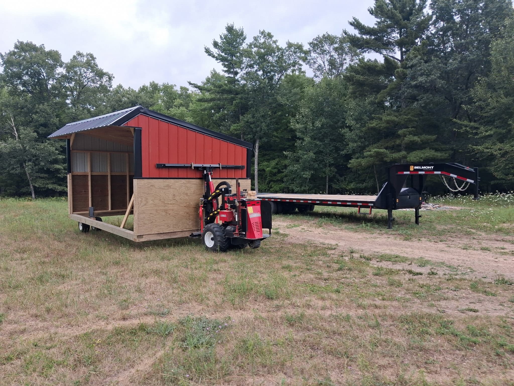 Red horse shelter beside equipment and a flatbed trailer.