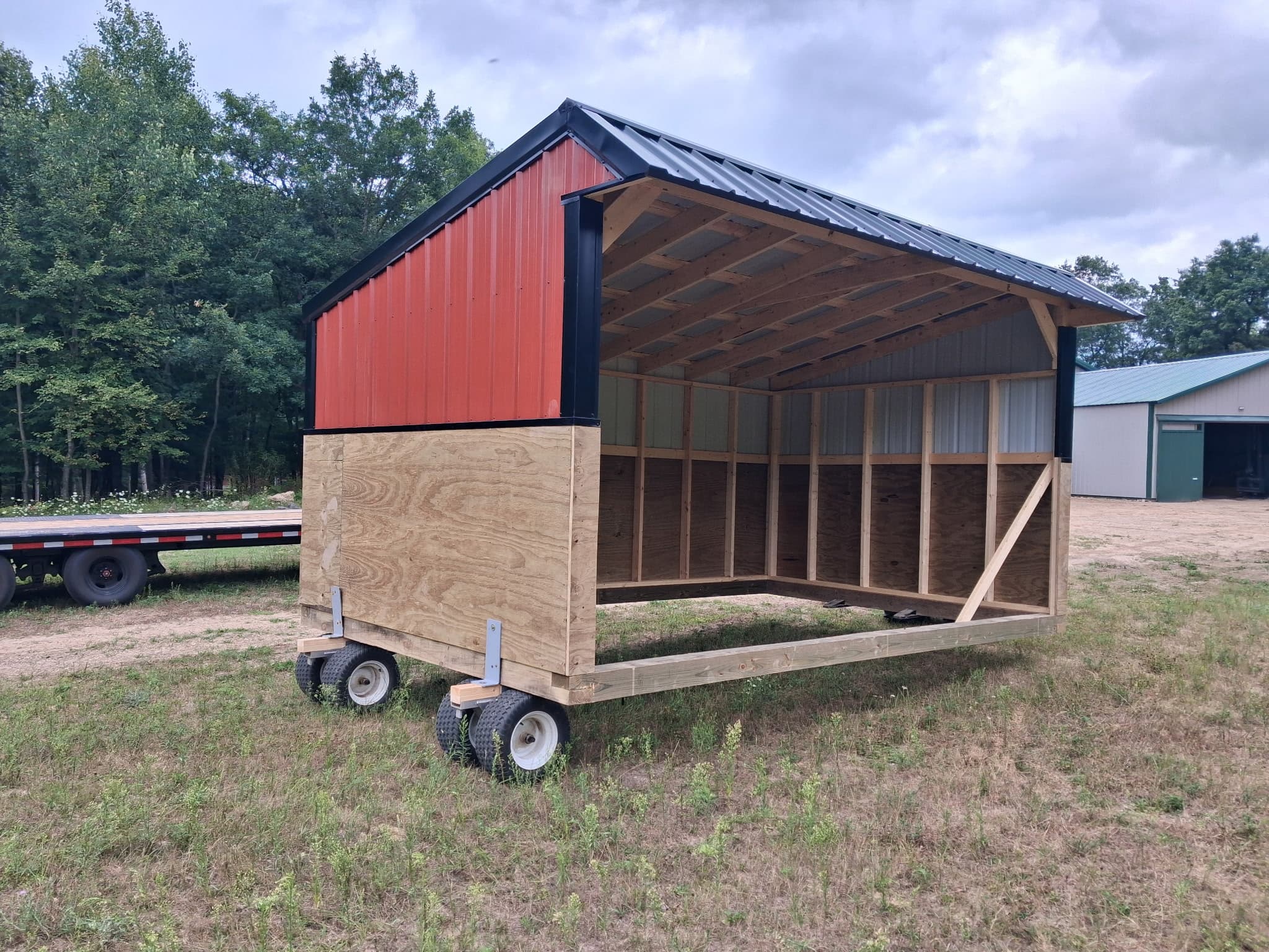 Red and black mobile horse shelter on wheels in a grassy field.